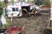 A worker with a excavator is operating for the levelled the ground just outside of renovating house