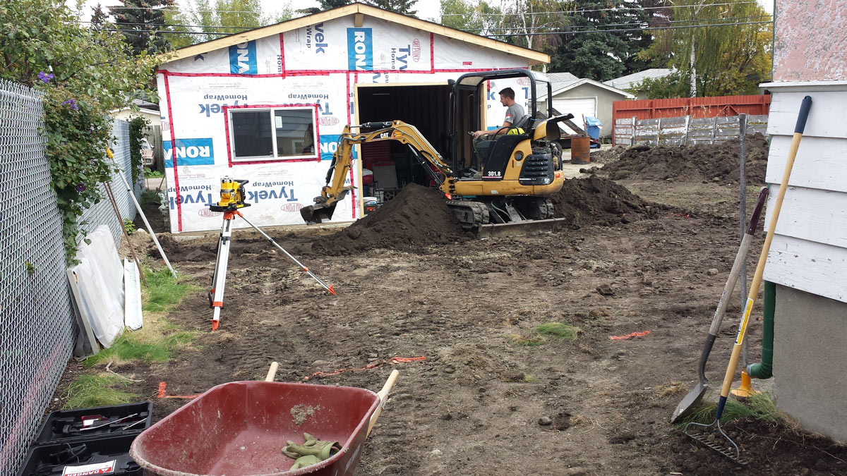 A worker with a excavator is operating for the levelled the ground just outside of renovating house