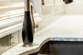 Modern brand new faucet over the marble counter top kitchen sink next to white shutter