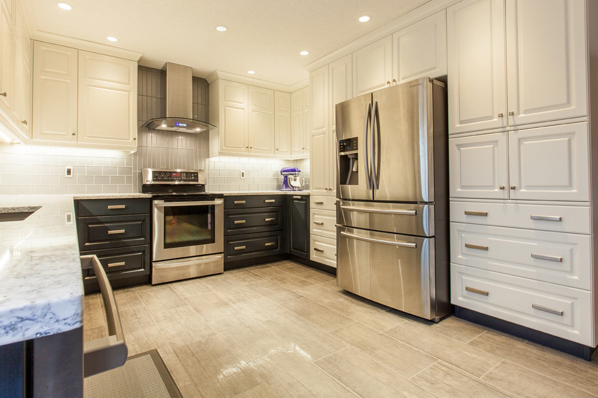 Modern Kitchen interior in beige colour and dark navy for the top and bottom closet with marble countertop and unique square shape ventilation fan and brand new double door fridge