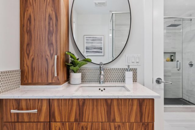 bathroom with wood veneer cabinet and round mirror above basin