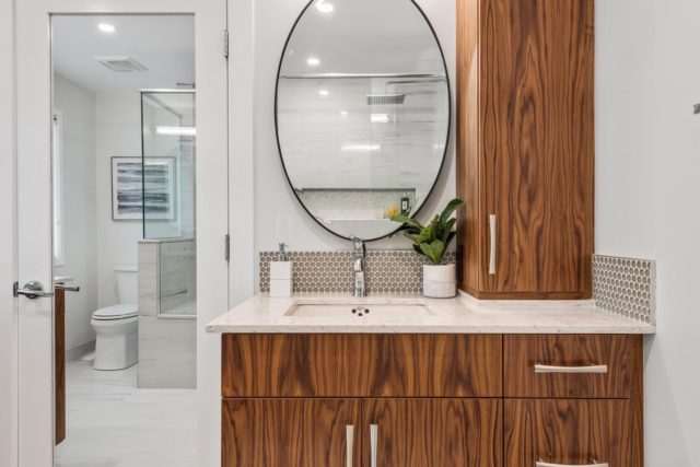 bathroom with wood veneer cabinet and round mirror above basin